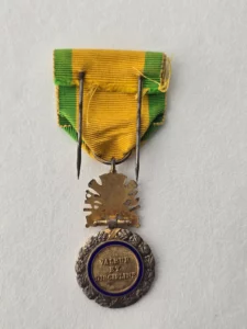 Médaille militaire 1870 «Valeur et Discipline» vue de dos, listel émaillé bleu, trophée d’armes doré, ruban jaune vert
