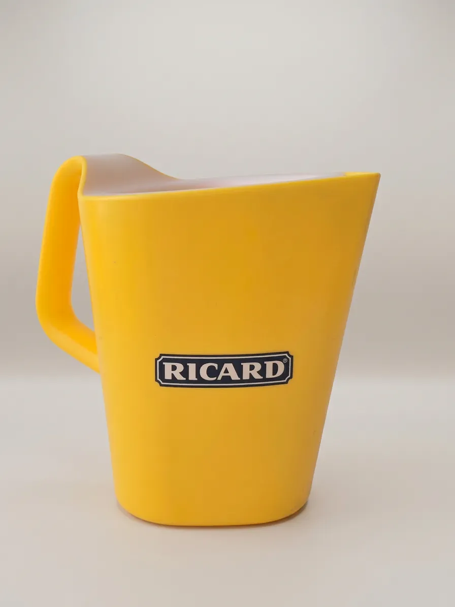 Pichet Ricard jaune publicitaire en plastique, vue latérale avec poignée, logo Ricard noir sur fond blanc, sur fond neutre.