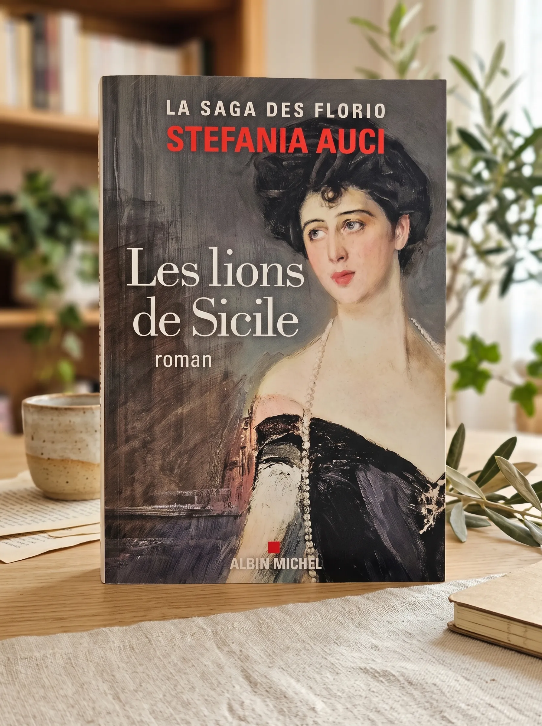 Livre Les lions de Sicile de Stefania Auci posé sur une table en bois avec une tasse de thé et des plantes en arrière-plan. Roman historique publié aux éditions Albin Michel.